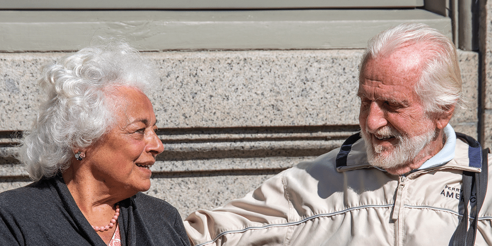 To pensionister sidder udendørs på en bænk og snakker